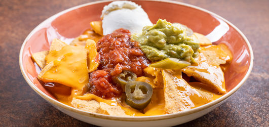 Mexican Nachos served with jalapenos, melted cheese, sour cream and guacamole on a plate