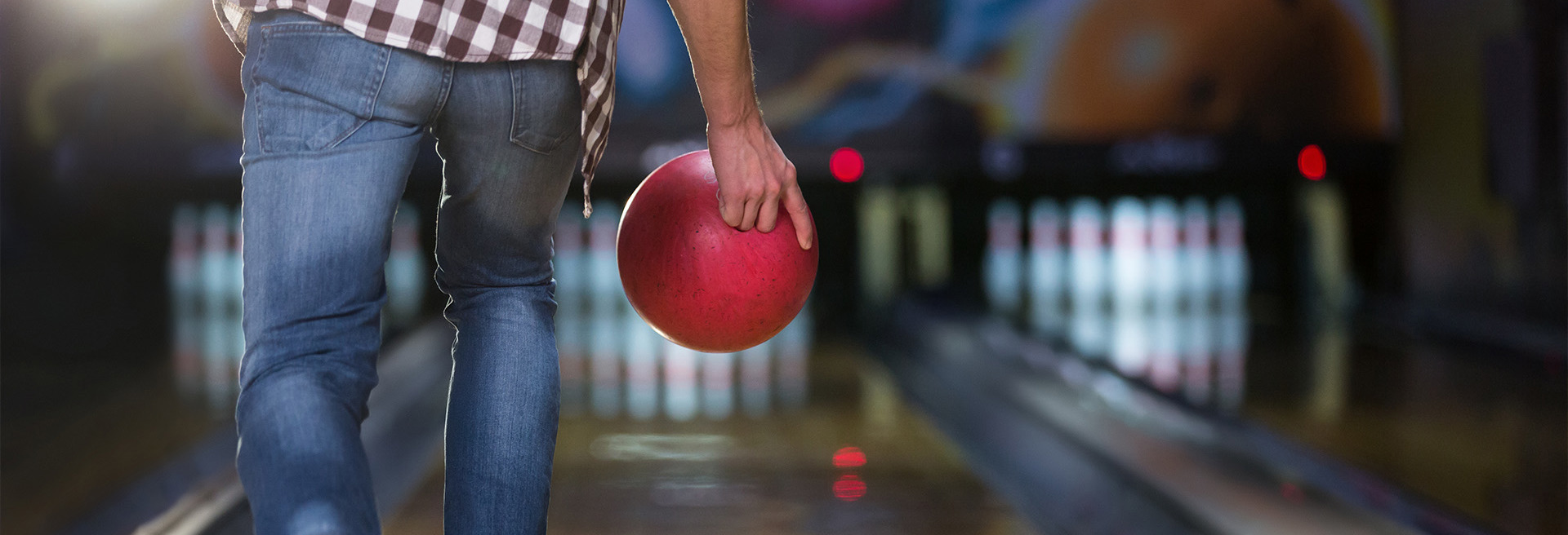 Male proceeding to throw a red bowling ball down a polished lane